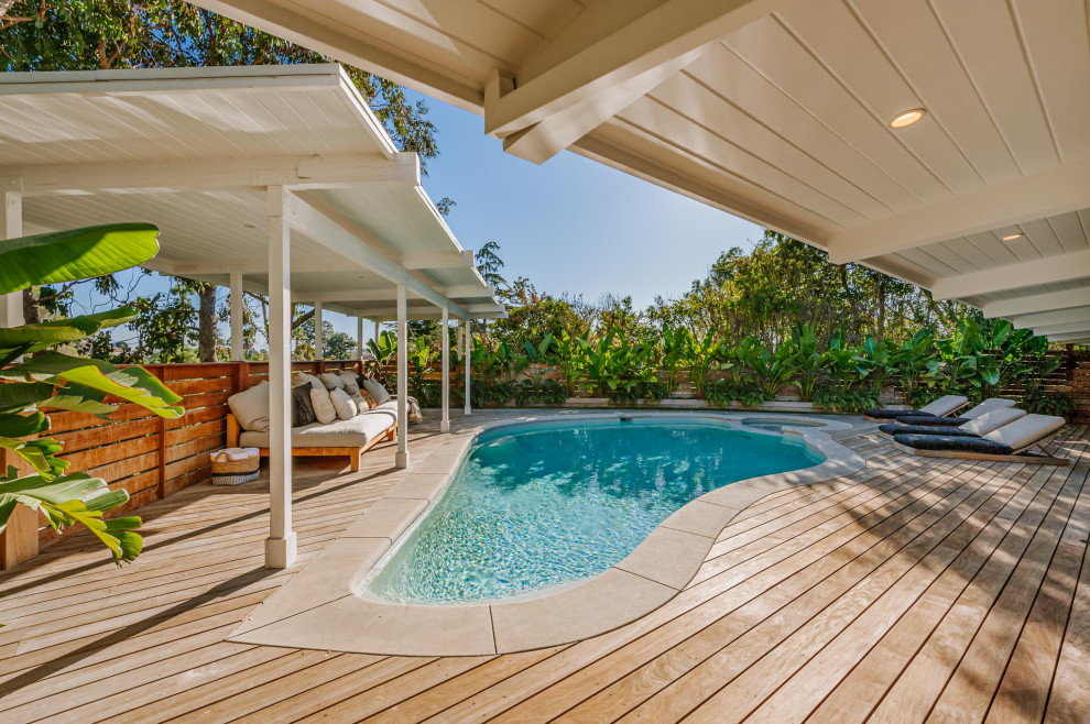 Large midcentury backyard custom-shaped natural pool in Los Angeles with a hot tub and decking.