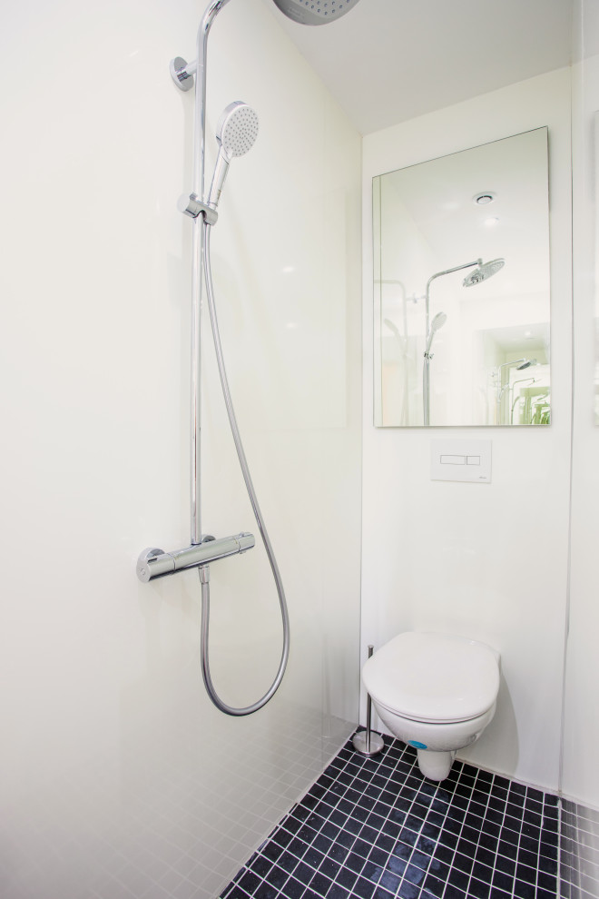 Réalisation d'une petite salle d'eau nordique avec une douche à l'italienne, WC suspendus, un mur blanc, un sol en carrelage de céramique, un sol noir, une cabine de douche à porte battante et meuble-lavabo suspendu.
