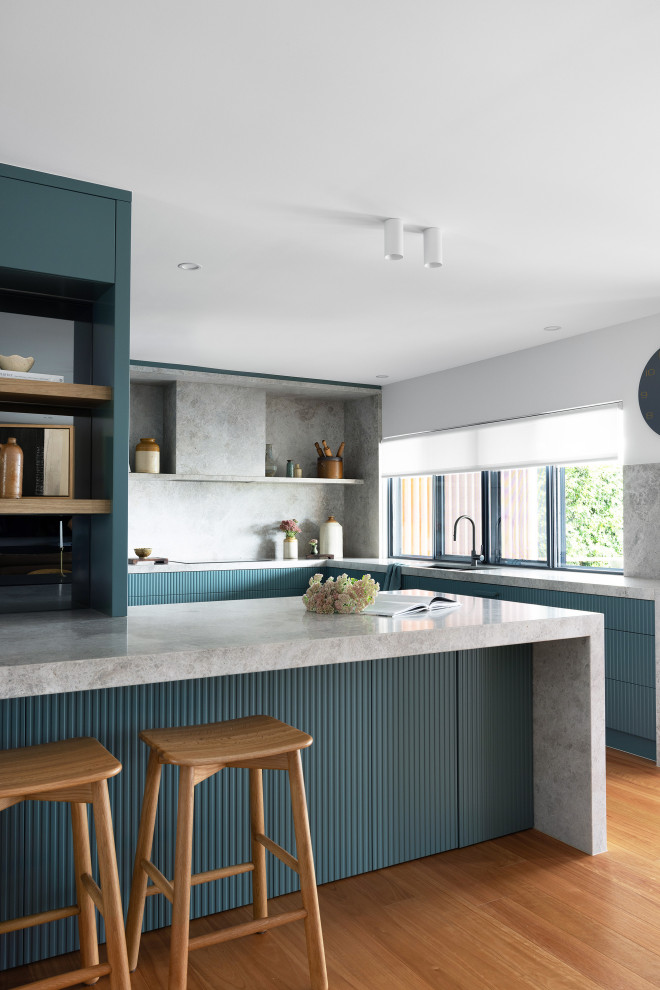 Inredning av ett modernt grå grått l-kök, med en undermonterad diskho, släta luckor, blå skåp, grått stänkskydd, stänkskydd i sten, mellanmörkt trägolv, en halv köksö och brunt golv