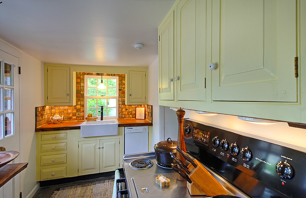 Photo of a small eclectic u-shaped separate kitchen in Philadelphia with a farmhouse sink, raised-panel cabinets, yellow cabinets, wood benchtops, white splashback, white appliances, slate floors and no island.