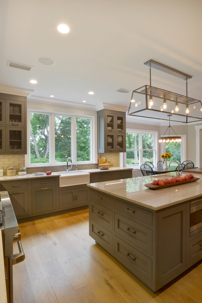 Photo of an expansive traditional u-shaped eat-in kitchen in New York with a farmhouse sink, recessed-panel cabinets, grey cabinets, quartzite benchtops, beige splashback, brick splashback, stainless steel appliances, light hardwood floors, with island, beige floor and multi-coloured benchtop.