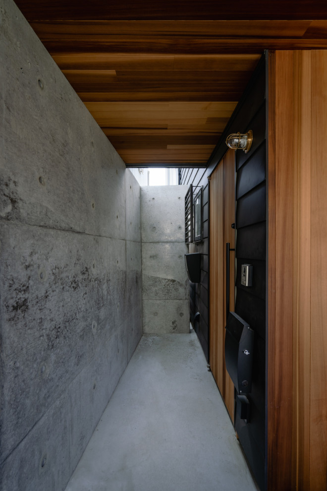 Idee per una porta d'ingresso moderna con pareti nere, pavimento in cemento, una porta singola, una porta in legno bruno, pavimento grigio e soffitto in legno