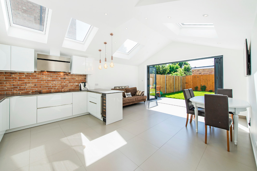 This is an example of a contemporary u-shaped open plan kitchen in Other with flat-panel cabinets, white cabinets, stainless steel benchtops and a peninsula.
