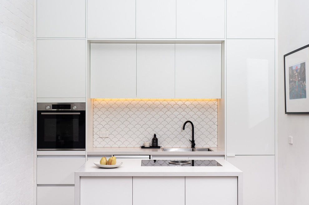 Photo of a mid-sized modern u-shaped kitchen pantry in Melbourne with a drop-in sink, open cabinets, white cabinets, solid surface benchtops, white splashback, mosaic tile splashback, stainless steel appliances, with island, beige floor, medium hardwood floors and white benchtop.
