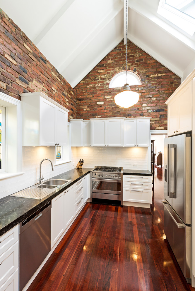 This is an example of a small single-wall separate kitchen in Melbourne with a double-bowl sink, white cabinets, wood benchtops, white splashback, timber splashback, stainless steel appliances, laminate floors and brown floor.