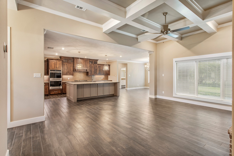 Large arts and crafts open concept living room in Other with a home bar, beige walls, ceramic floors, a standard fireplace, a brick fireplace surround, a wall-mounted tv, brown floor and coffered.