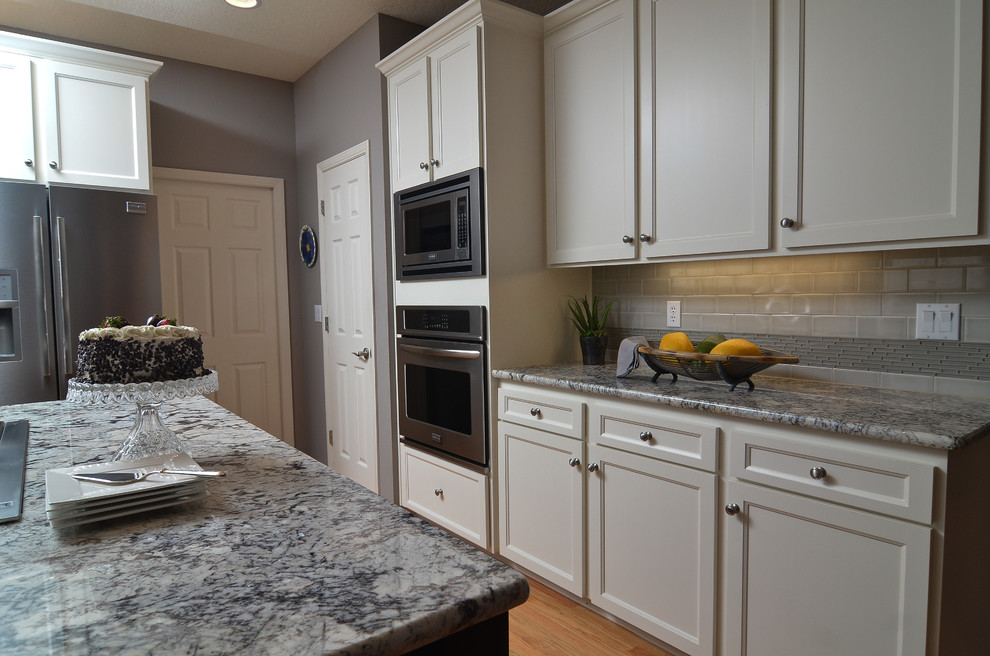 This is an example of a mid-sized transitional eat-in kitchen in Portland with shaker cabinets, white cabinets, granite benchtops, grey splashback, porcelain splashback, stainless steel appliances, medium hardwood floors and with island.
