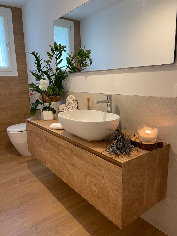This is an example of a small contemporary master bathroom in Venice with light wood cabinets, a one-piece toilet, beige tile, porcelain tile, porcelain floors, a vessel sink, wood benchtops, brown floor, a single vanity and a floating vanity.