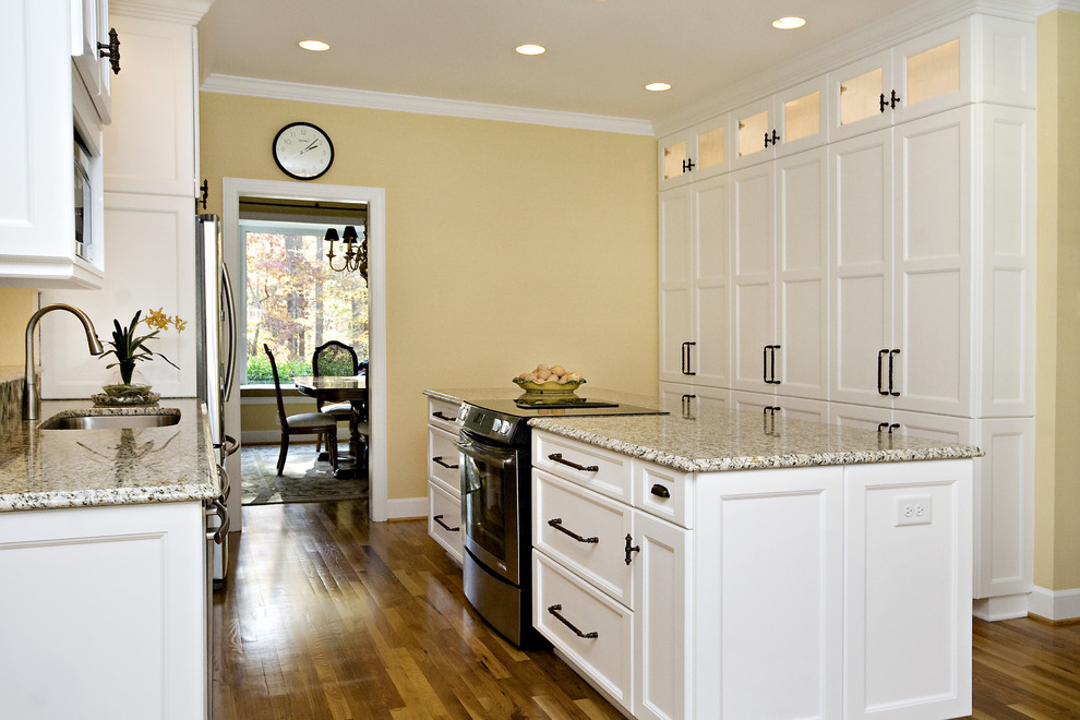 Inspiration for a mid-sized transitional galley eat-in kitchen in Raleigh with an undermount sink, recessed-panel cabinets, white cabinets, granite benchtops, multi-coloured splashback, glass tile splashback, stainless steel appliances, medium hardwood floors, with island, orange floor and multi-coloured benchtop.