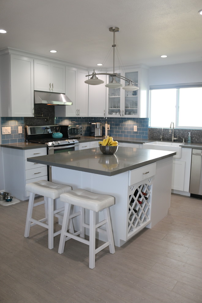 This is an example of a mid-sized contemporary u-shaped eat-in kitchen in San Diego with a farmhouse sink, shaker cabinets, white cabinets, solid surface benchtops, blue splashback, glass tile splashback, stainless steel appliances, ceramic floors and with island.