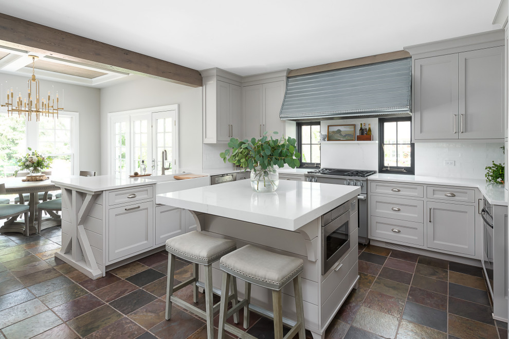 Photo of a mid-sized country u-shaped eat-in kitchen in Chicago with a farmhouse sink, grey cabinets, quartz benchtops, white splashback, subway tile splashback, panelled appliances, slate floors, with island, white benchtop and recessed-panel cabinets.