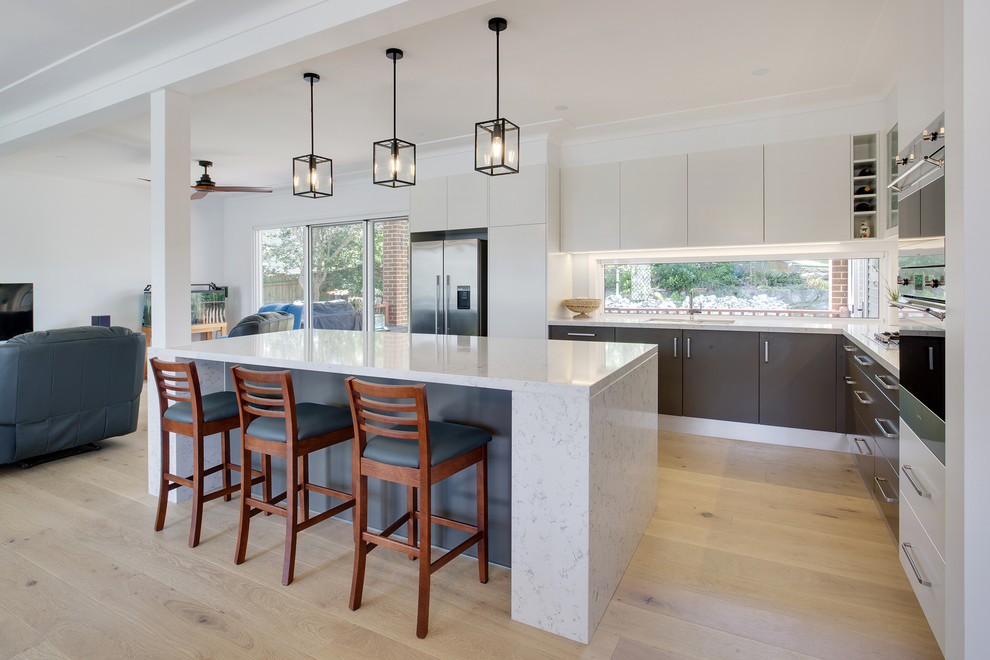 Inspiration for a large modern l-shaped open plan kitchen in Sydney with an undermount sink, flat-panel cabinets, white cabinets, quartz benchtops, white splashback, glass sheet splashback, stainless steel appliances, light hardwood floors, with island and grey benchtop.