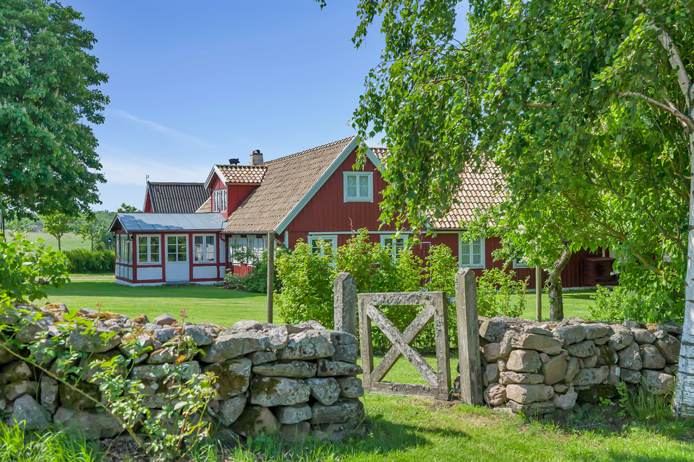 Expansive country two-storey red exterior in Malmo with stone veneer and a gable roof.