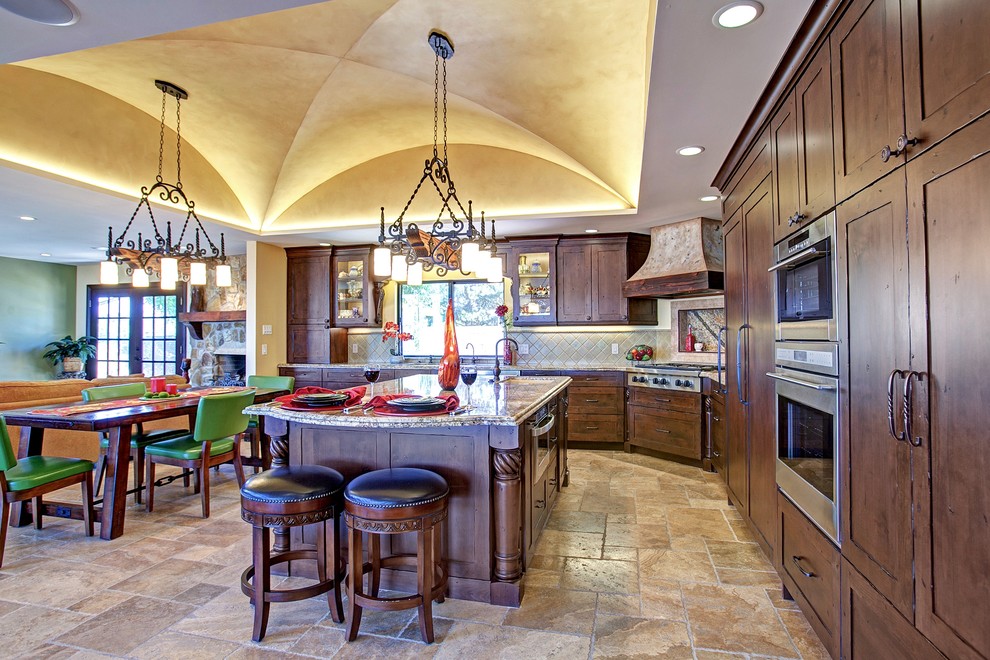 Inspiration for a mid-sized mediterranean l-shaped open plan kitchen in San Diego with with island, recessed-panel cabinets, brown cabinets, granite benchtops, green splashback, ceramic splashback, stainless steel appliances, travertine floors and beige floor.