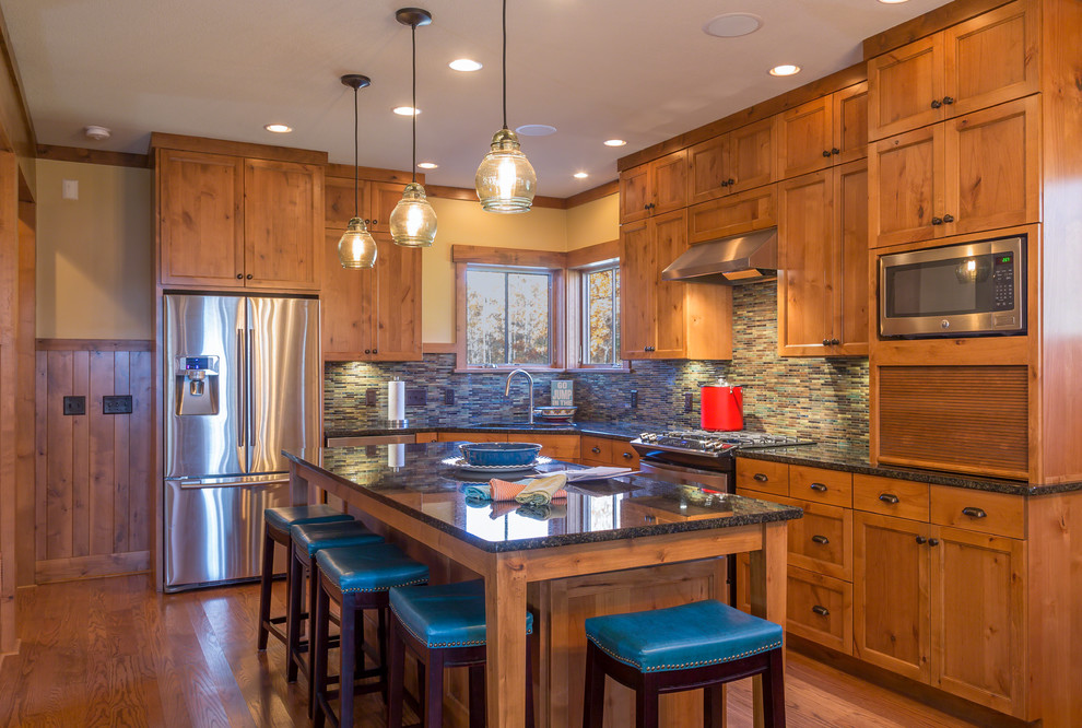This is an example of a mid-sized country l-shaped eat-in kitchen in Minneapolis with an undermount sink, shaker cabinets, medium wood cabinets, quartz benchtops, multi-coloured splashback, glass tile splashback, stainless steel appliances, medium hardwood floors and with island.