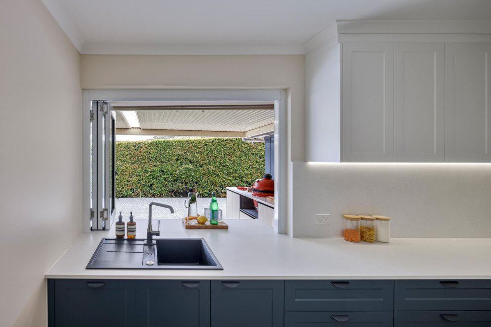 Cette image montre une arrière-cuisine design avec un évier 2 bacs, un placard à porte shaker, des portes de placard bleues, une crédence beige, une crédence en travertin, un électroménager noir et un plan de travail beige.