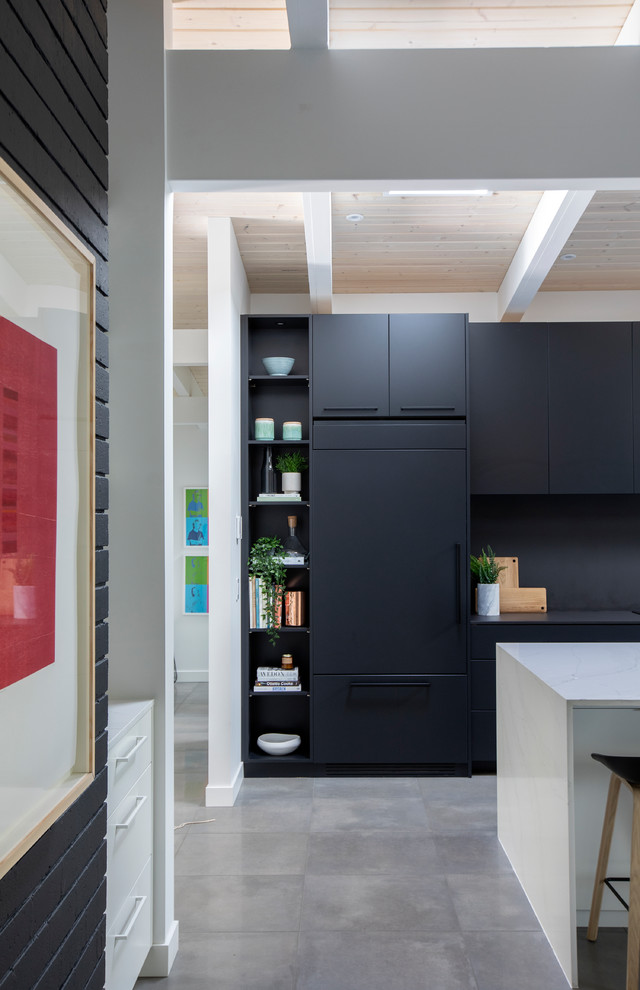 Large midcentury single-wall open plan kitchen in Vancouver with flat-panel cabinets, black cabinets, quartz benchtops, black splashback, with island, grey floor, an undermount sink, panelled appliances, concrete floors and black benchtop.