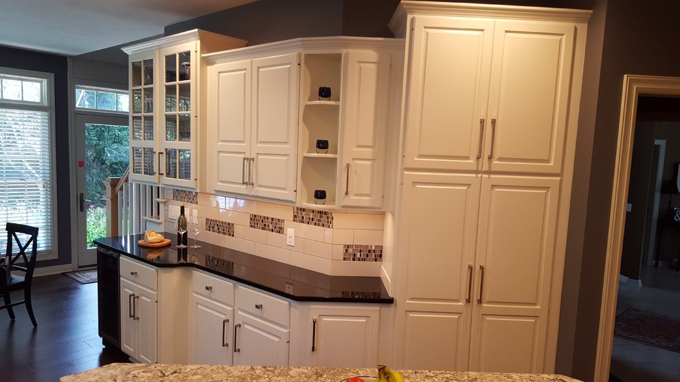 Inspiration for a mid-sized transitional l-shaped medium tone wood floor and brown floor kitchen remodel with an undermount sink, raised-panel cabinets, white cabinets, granite countertops, white backsplash, subway tile backsplash, stainless steel appliances and an island