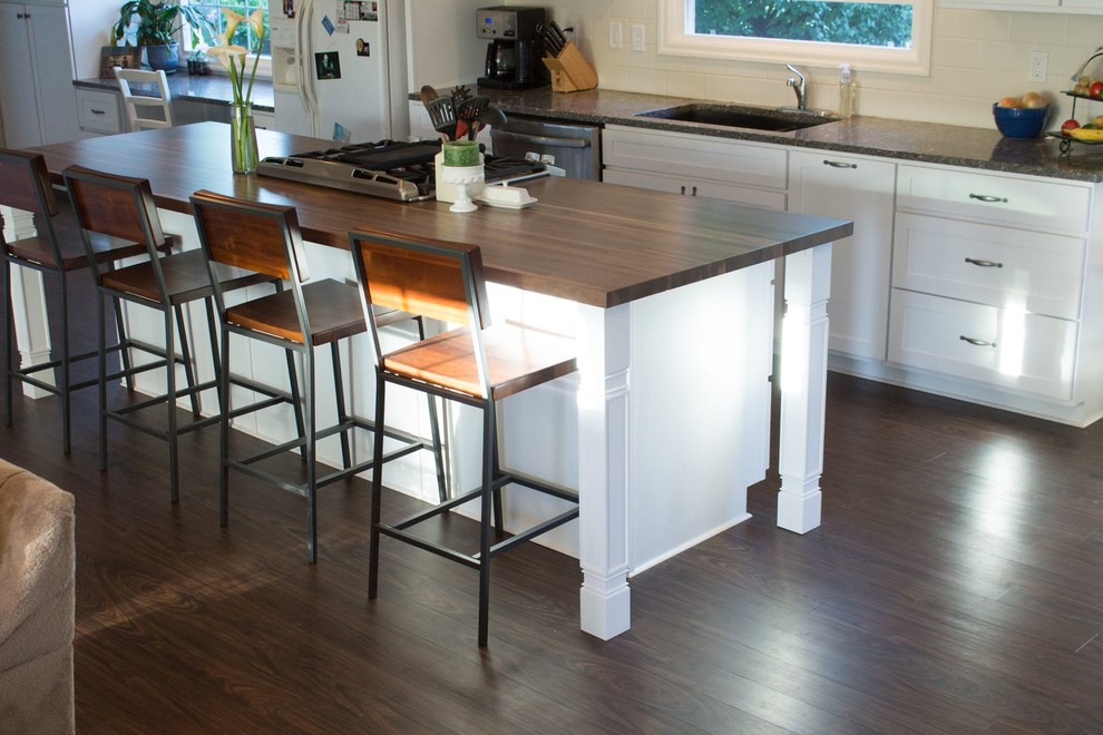 Inspiration for a mid-sized transitional galley dark wood floor and brown floor open concept kitchen remodel with an undermount sink, shaker cabinets, white cabinets, wood countertops, white backsplash, porcelain backsplash, white appliances and an island