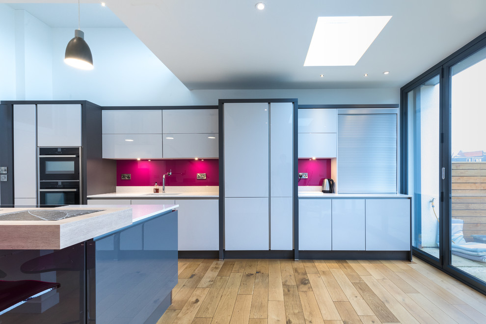 Design ideas for a large contemporary eat-in kitchen in Hampshire with an integrated sink, flat-panel cabinets, grey cabinets, quartzite benchtops, pink splashback, glass tile splashback, panelled appliances, medium hardwood floors and with island.