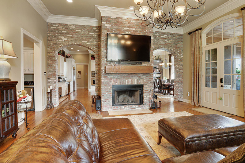 Photo of a large traditional open concept living room in New Orleans with beige walls, light hardwood floors, a standard fireplace, a brick fireplace surround and a wall-mounted tv.