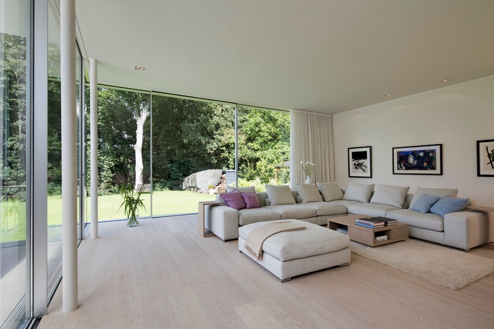 This is an example of a contemporary open concept living room in Hamburg with white walls and light hardwood floors.