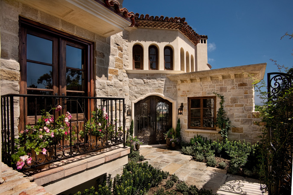 Design ideas for a large mediterranean split-level beige house exterior in San Diego with stone veneer, a flat roof and a tile roof.