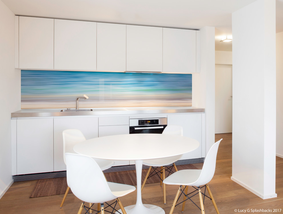 Design ideas for a small beach style separate kitchen in Sunshine Coast with an integrated sink, stainless steel benchtops, blue splashback, glass sheet splashback, stainless steel appliances, medium hardwood floors and brown floor.
