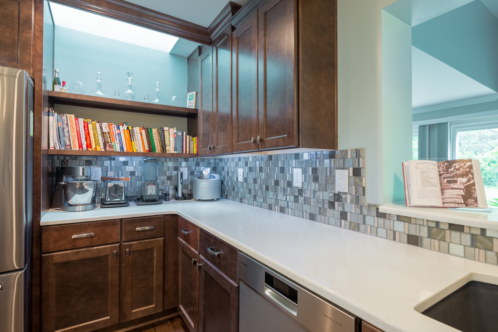 Example of a mid-sized dark wood floor eat-in kitchen design with shaker cabinets, brown cabinets, glass tile backsplash, stainless steel appliances and an island