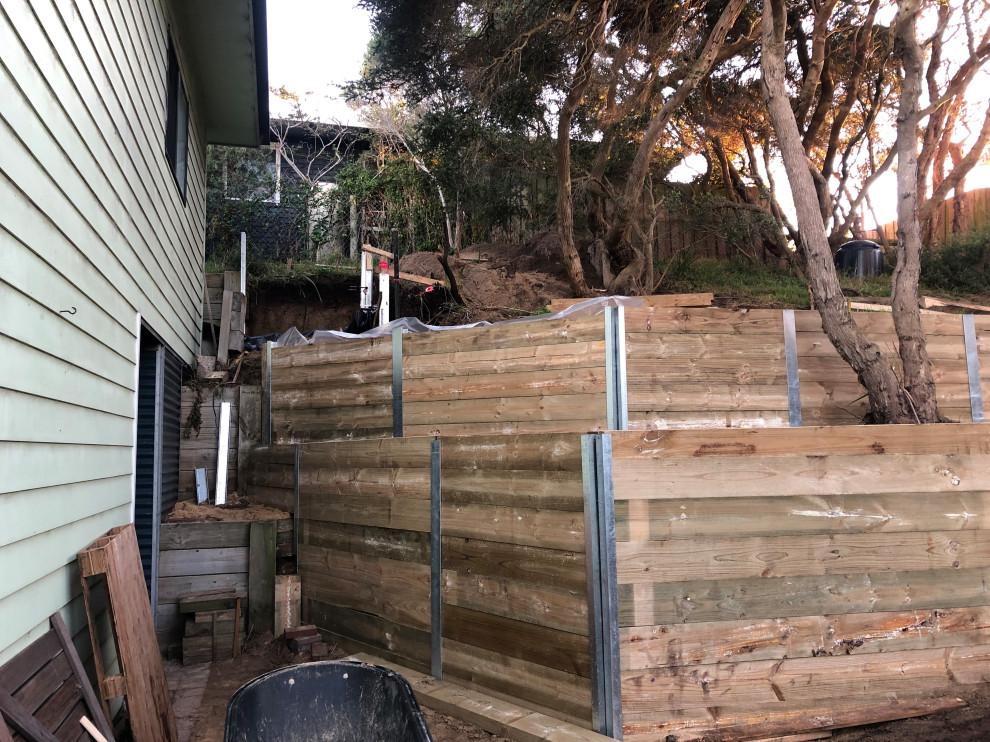 This is an example of an expansive contemporary back formal fully shaded garden for summer in Melbourne with a retaining wall and a wood fence.