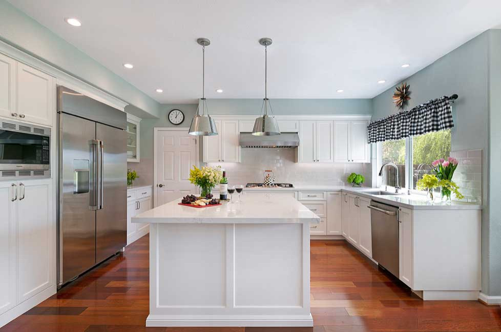 Mid-sized elegant l-shaped medium tone wood floor and brown floor open concept kitchen photo in San Francisco with an undermount sink, recessed-panel cabinets, white cabinets, quartz countertops, gray backsplash, subway tile backsplash, stainless steel appliances, an island and white countertops