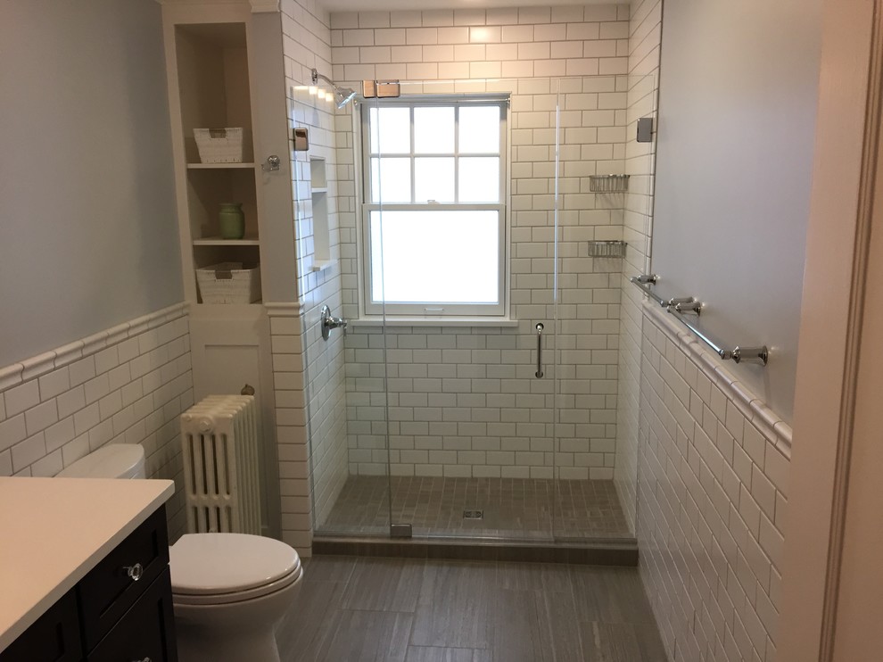 This is an example of a mid-sized transitional 3/4 bathroom in Cleveland with shaker cabinets, dark wood cabinets, an alcove shower, a two-piece toilet, white tile, porcelain tile, porcelain floors, an undermount sink and engineered quartz benchtops.