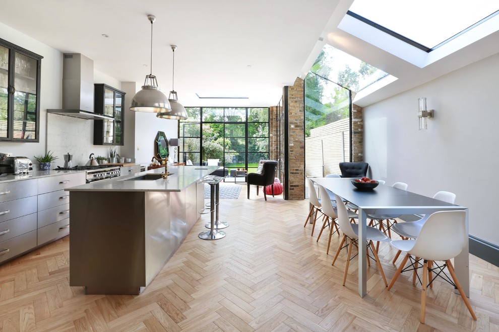 Photo of a large contemporary single-wall eat-in kitchen in London with a double-bowl sink, flat-panel cabinets, stainless steel cabinets, marble benchtops, white splashback, marble splashback, stainless steel appliances, light hardwood floors, a peninsula and beige floor.