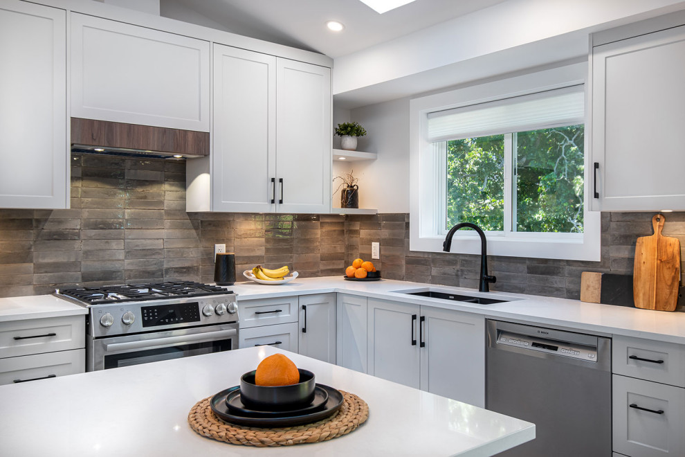 Open concept kitchen - mid-sized transitional u-shaped laminate floor and brown floor open concept kitchen idea in Vancouver with an undermount sink, shaker cabinets, white cabinets, quartz countertops, gray backsplash, porcelain backsplash, stainless steel appliances, an island and white countertops