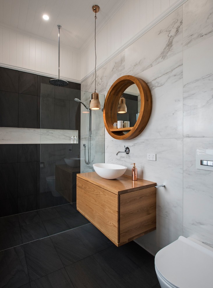 Contemporary 3/4 bathroom in Brisbane with medium wood cabinets, a wall-mount toilet, gray tile, black tile, ceramic tile, white walls, ceramic floors, a vessel sink, wood benchtops, an open shower, flat-panel cabinets, a curbless shower, black floor and brown benchtops.