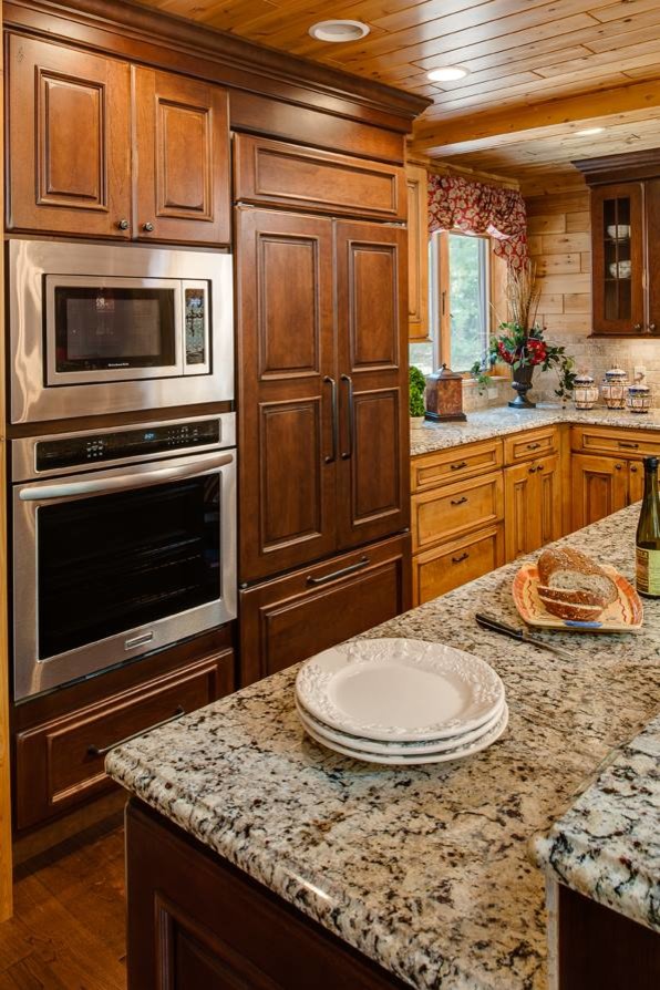 This is an example of a mid-sized country l-shaped open plan kitchen in Miami with a farmhouse sink, raised-panel cabinets, dark wood cabinets, granite benchtops, beige splashback, stone tile splashback, panelled appliances, medium hardwood floors, with island, brown floor and grey benchtop.