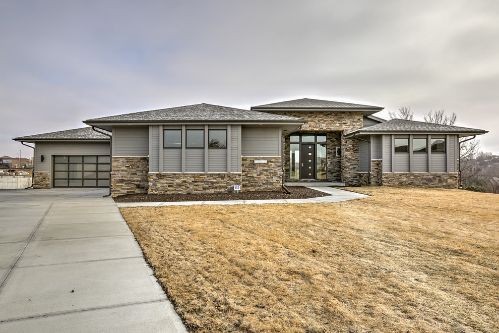 This is an example of a large contemporary split-level grey house exterior in Omaha with mixed siding.