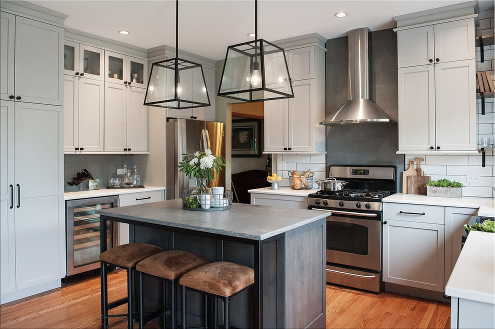 This is an example of a mid-sized industrial u-shaped eat-in kitchen in Chicago with a farmhouse sink, shaker cabinets, grey cabinets, quartz benchtops, white splashback, ceramic splashback, stainless steel appliances, light hardwood floors, with island, beige floor and grey benchtop.