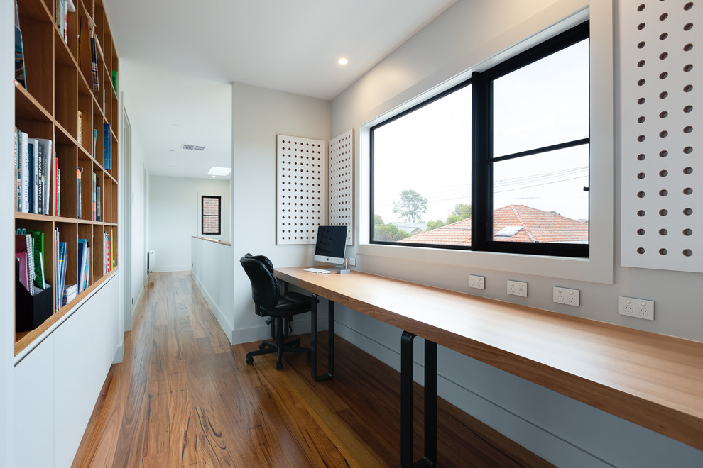 Design ideas for a small contemporary study room in Melbourne with white walls, medium hardwood floors, a built-in desk and brown floor.