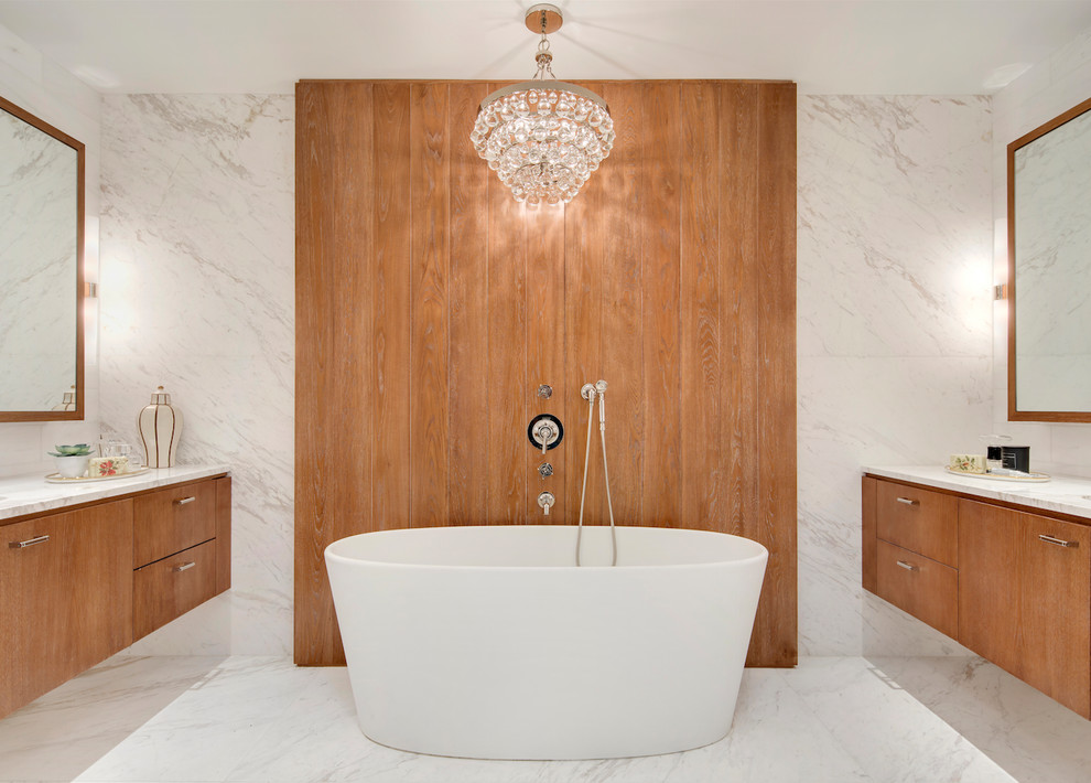 Photo of a contemporary master bathroom in New York with flat-panel cabinets, medium wood cabinets, a freestanding tub, white tile, stone slab, marble floors, marble benchtops and white floor.