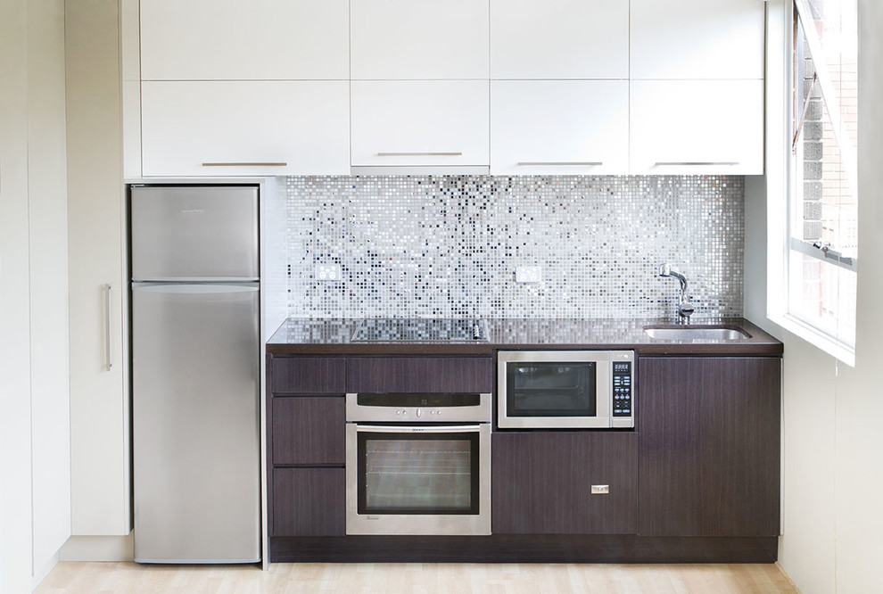 This is an example of a small modern single-wall open plan kitchen in Sydney with an undermount sink, flat-panel cabinets, brown cabinets, marble benchtops, metallic splashback, metal splashback, stainless steel appliances, bamboo floors, beige floor, brown benchtop and recessed.