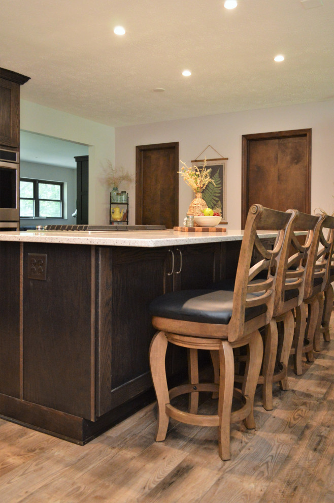 Mid-sized country l-shaped open plan kitchen in Chicago with an undermount sink, shaker cabinets, dark wood cabinets, quartzite benchtops, stainless steel appliances, laminate floors, with island, brown floor and grey benchtop.