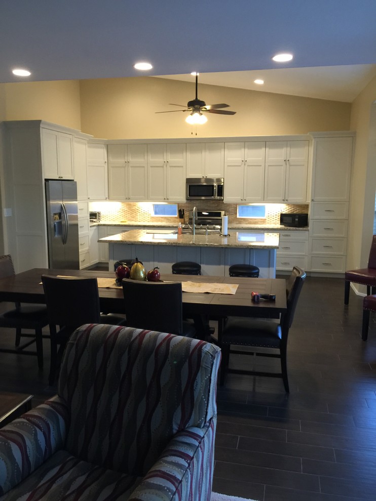 Example of a mid-sized transitional l-shaped porcelain tile and black floor open concept kitchen design in Phoenix with an undermount sink, recessed-panel cabinets, white cabinets, granite countertops, beige backsplash, stainless steel appliances and an island