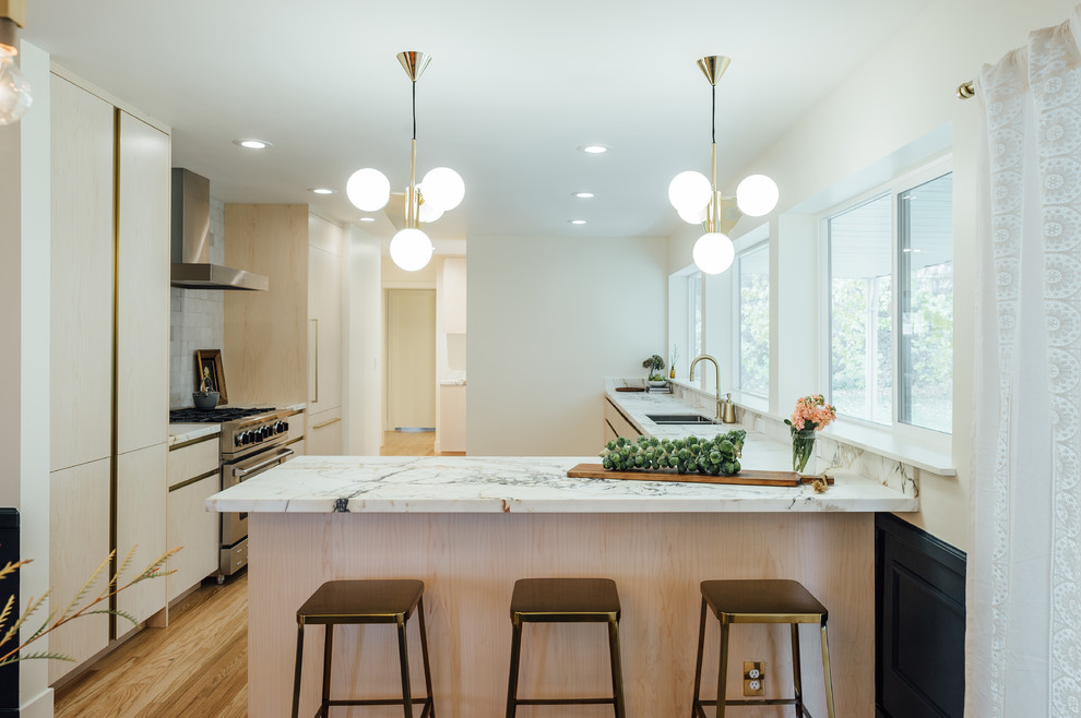 Design ideas for a mid-sized eclectic l-shaped eat-in kitchen in Salt Lake City with a drop-in sink, flat-panel cabinets, light wood cabinets, marble benchtops, white splashback, ceramic splashback, stainless steel appliances, medium hardwood floors and a peninsula.