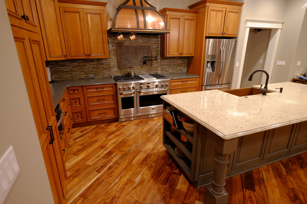 Large arts and crafts l-shaped eat-in kitchen in Sacramento with a farmhouse sink, shaker cabinets, medium wood cabinets, solid surface benchtops, brown splashback, stone tile splashback, stainless steel appliances, medium hardwood floors, with island and brown floor.
