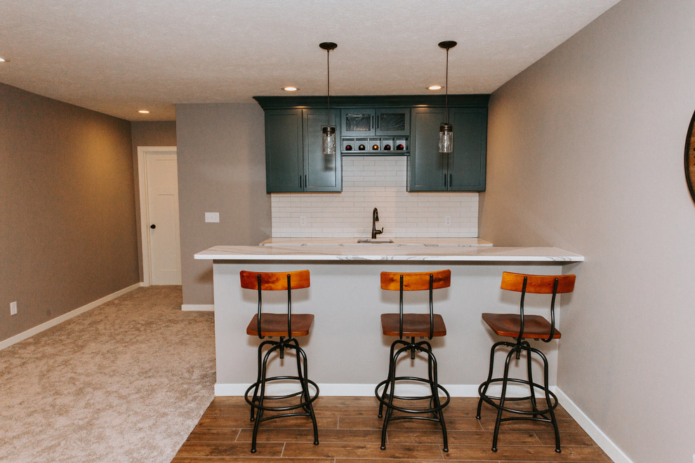 Small transitional galley seated home bar in Omaha with green cabinets, an undermount sink, shaker cabinets, marble benchtops, white splashback, subway tile splashback, medium hardwood floors, brown floor and white benchtop.