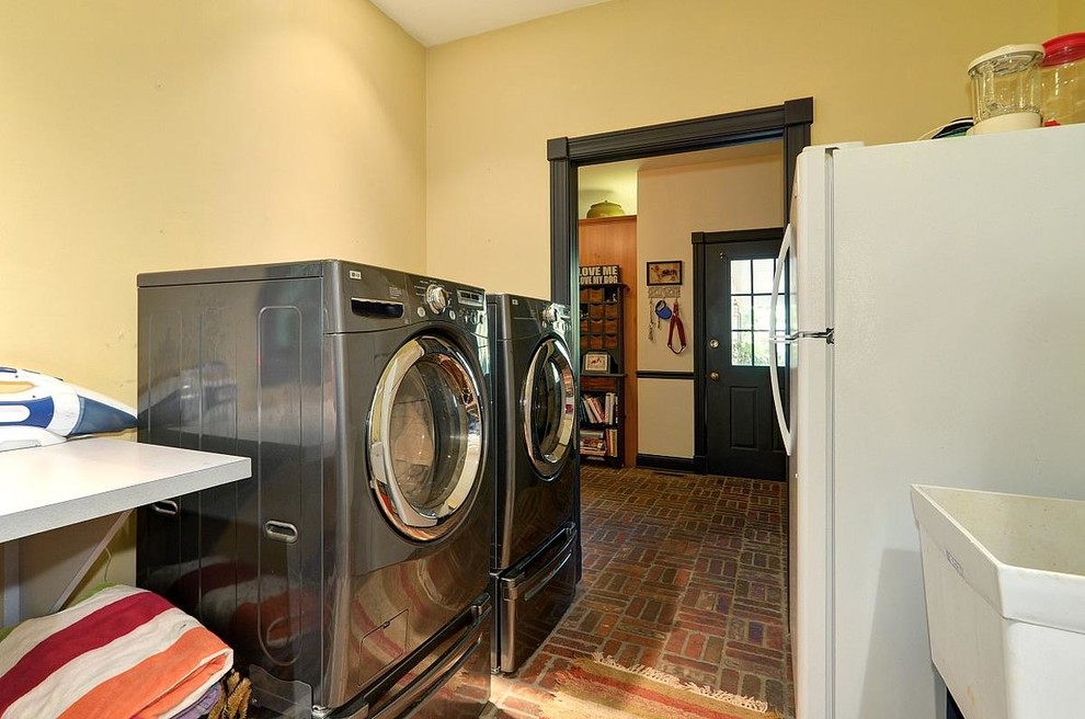 Photo of a mid-sized country galley dedicated laundry room in Milwaukee with an utility sink, recessed-panel cabinets, medium wood cabinets, laminate benchtops, yellow walls, brick floors and a side-by-side washer and dryer.