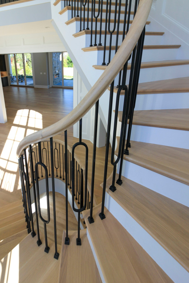 Modelo de escalera curva clásica renovada extra grande con escalones de madera, contrahuellas de madera, barandilla de varios materiales y boiserie