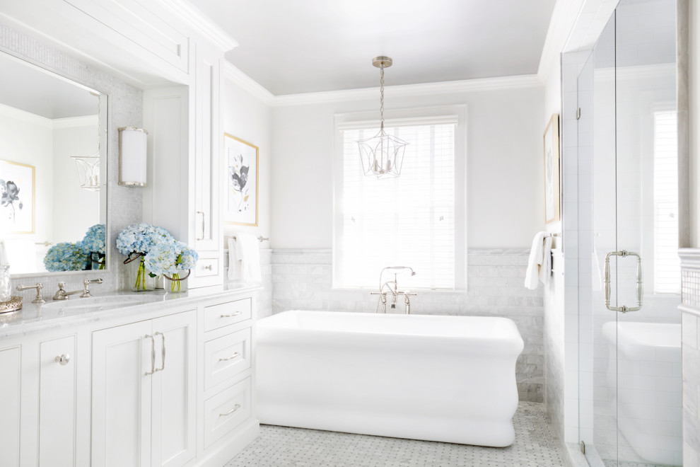 Cette image montre une salle de bain principale et grise et blanche traditionnelle avec un placard avec porte à panneau encastré, des portes de placard blanches, une baignoire indépendante, une douche, un carrelage gris, du carrelage en marbre, un mur blanc, un sol en marbre, un lavabo encastré, un plan de toilette en marbre, un sol gris, une cabine de douche à porte battante, un plan de toilette gris, meuble double vasque et meuble-lavabo encastré.