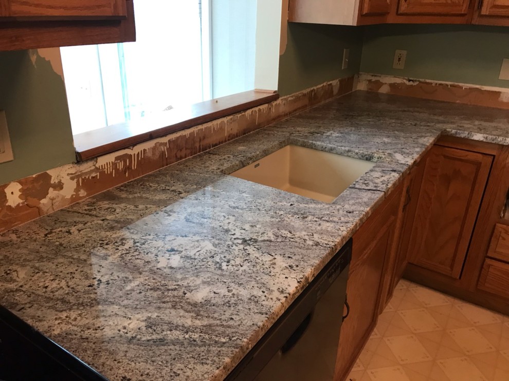 Mid-sized l-shaped separate kitchen in Other with an undermount sink, recessed-panel cabinets, medium wood cabinets, granite benchtops, black appliances, linoleum floors, a peninsula, beige floor and blue benchtop.
